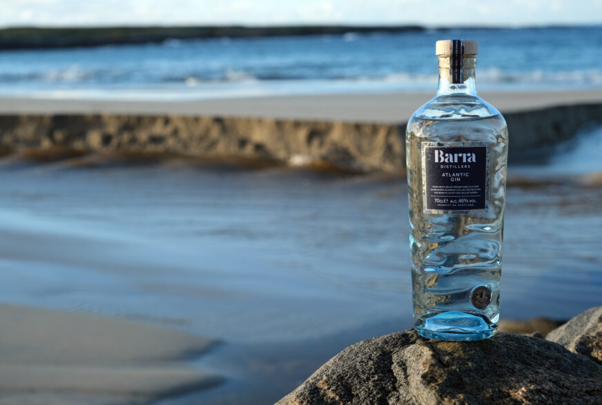 Isle of Barra Gin Atlantic Gin sustainable glass bottle made by Verallia. Picture of the bottle on the beach, with the bottle that feature sea-like embossing and mould