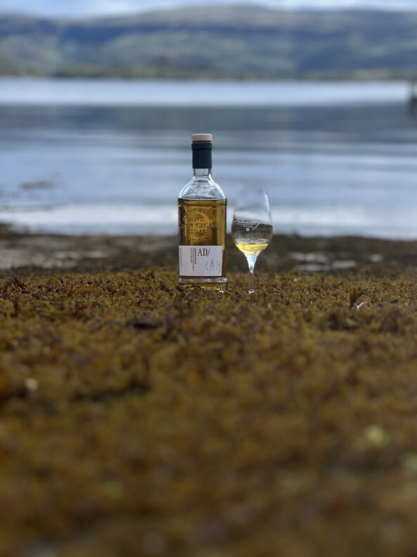 Ardnamurchan whisky glass bottle made by Verallia, set with a glass on the beach